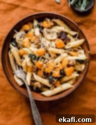 Butternut Squash Sausage Pasta 8 A brown bowl filled with Butternut Squash Mushroom Pasta that's topped with parmesan cheese, all on a burnt orange linen tablecloth.