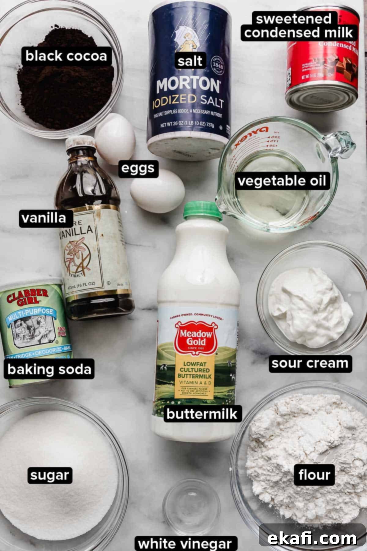 Όρεο Τρυπητό Κέικ 3 Συστατικά συνταγής Oreo Poke Cake σε λευκή μαρμάρινη επιφάνεια, τα συστατικά περιλαμβάνουν μαύρο κακάο, βουτυρόγαλα, ξινή κρέμα, αλεύρι, αλάτι, αυγά, λάδι και αλεύρι.