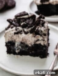 Όρεο Τρυπητό Κέικ 10 Μια φέτα από συνταγή Oreo Poke Cake σε λευκό πιάτο, το εύκολο κέικ Oreo σε ταψί διαθέτει μαύρη βάση κέικ, γλυκό συμπυκνωμένο γάλα και μια εύκολη επικάλυψη πουτίγκας Oreo.