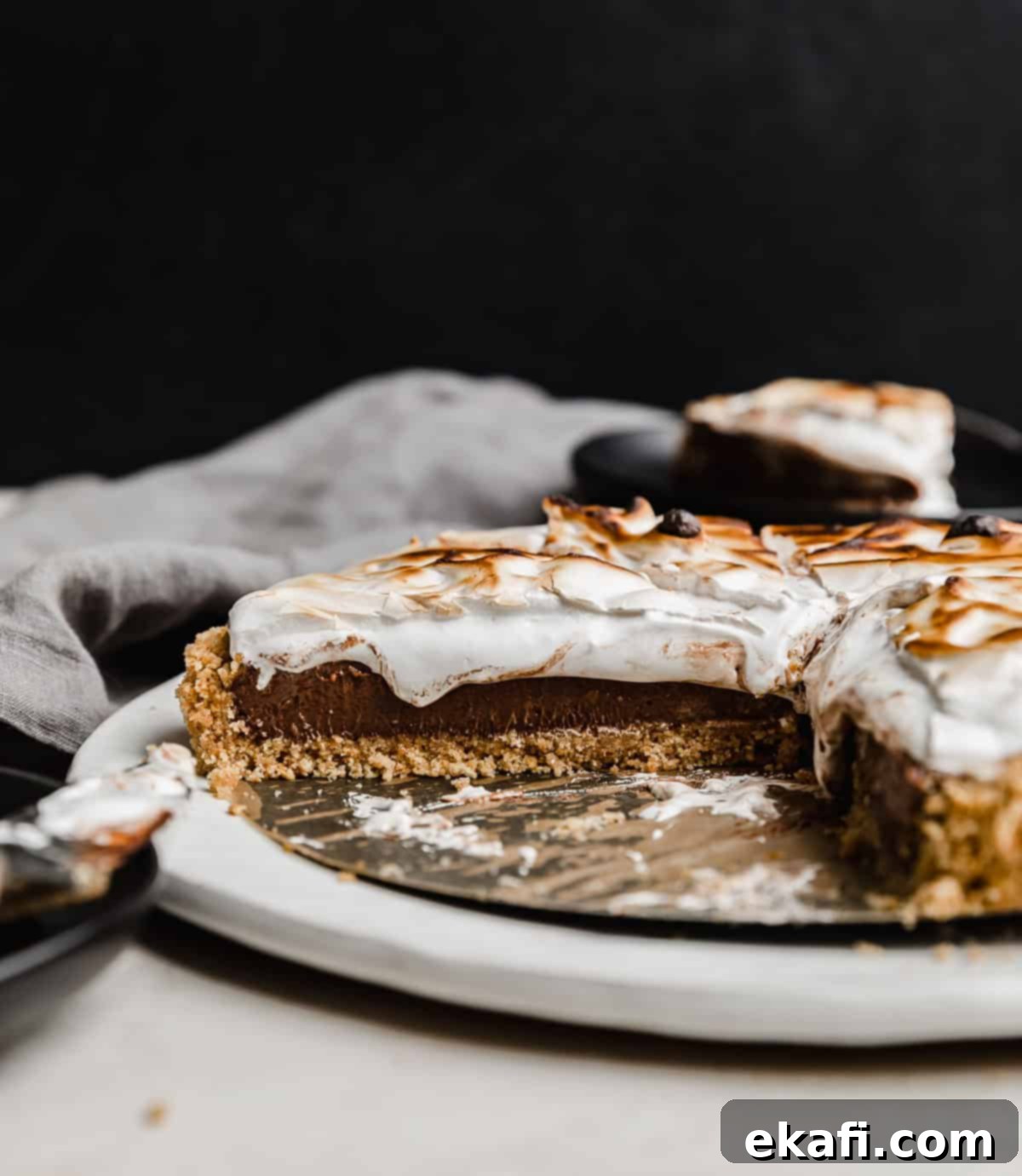 Σμόρς Τάρτα 8 Μια συνταγή S'mores Pie φτιαγμένη με βάση μπισκότου graham, πουτίγκα σοκολάτας και κρέμα marshmallow, πάνω σε μαύρο φόντο.