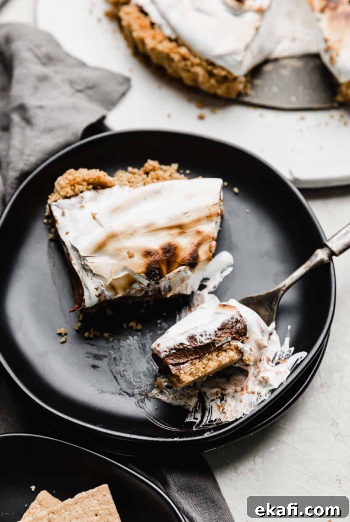 Σμόρς Τάρτα 9 Μια φέτα S'mores Pie σε μαύρο πιάτο με ένα πιρούνι να κόβει ένα κομμάτι.