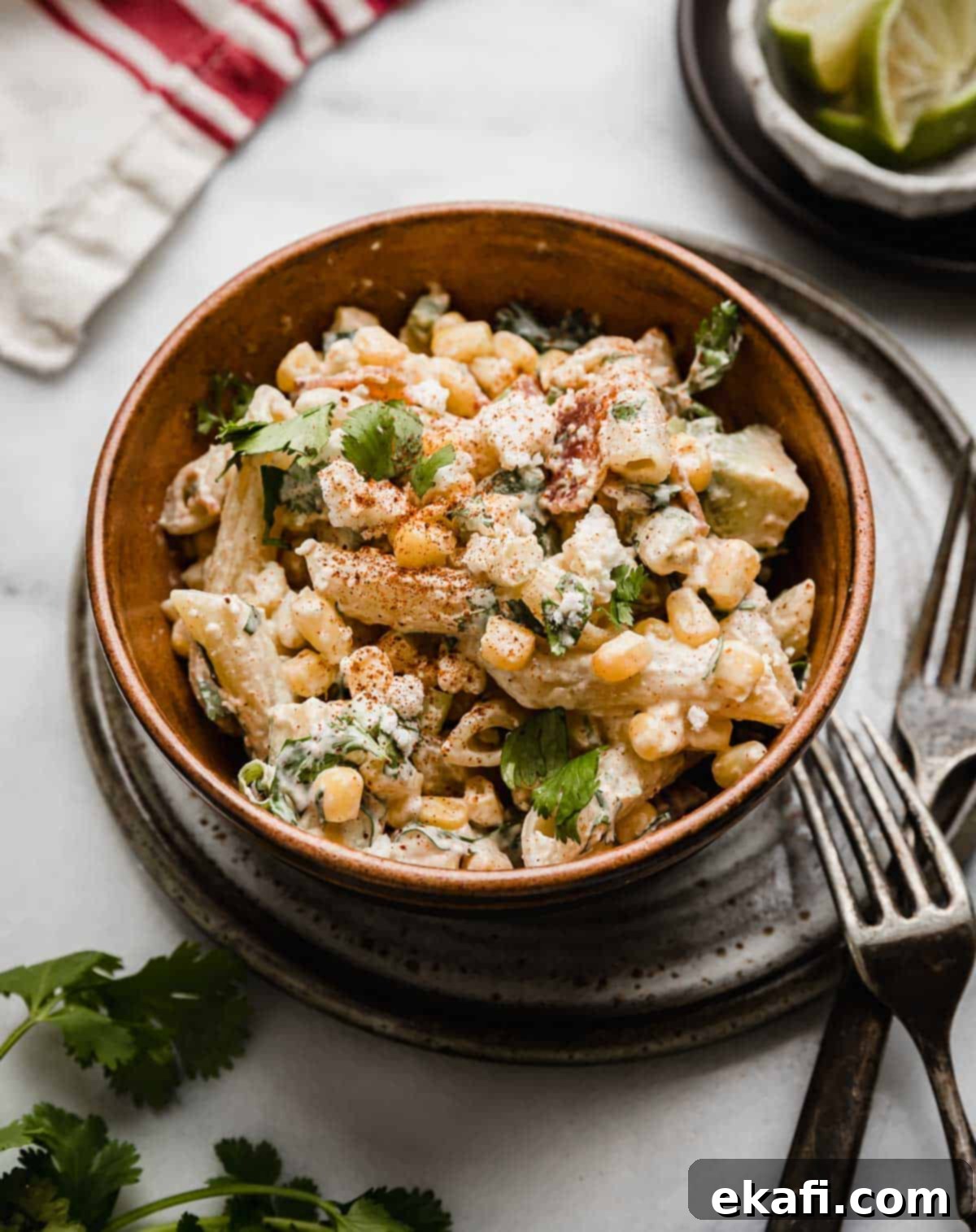 Elote Fiesta Pasta Salad 7 Mexican Street Corn Pasta Salad recipe in a brown bowl with two forks next to the bowl.