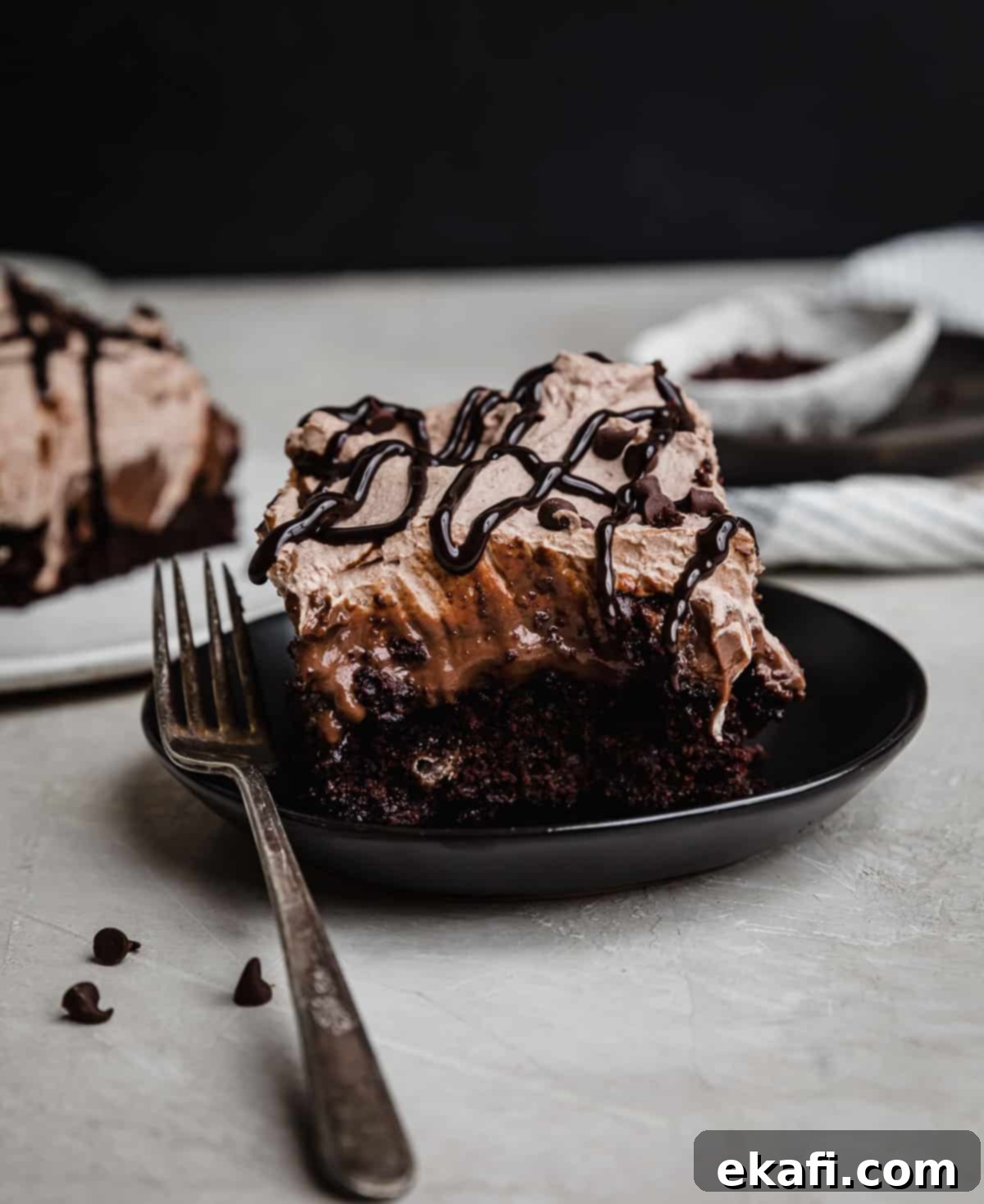 Chocolate Poke Cake 11 A beautifully presented Chocolate Pudding Poke Cake on a black plate, generously topped with fluffy chocolate whipped cream and a delicate drizzle of chocolate sauce, highlighting its elegant appeal.
