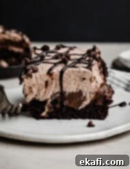 Chocolate Poke Cake 12 A luscious Triple Chocolate Poke Cake, featuring layers of moist cake, rich chocolate pudding, and fluffy chocolate whipped cream, beautifully drizzled with chocolate sauce and adorned with mini chocolate chips, presented on a white plate against a dark background.