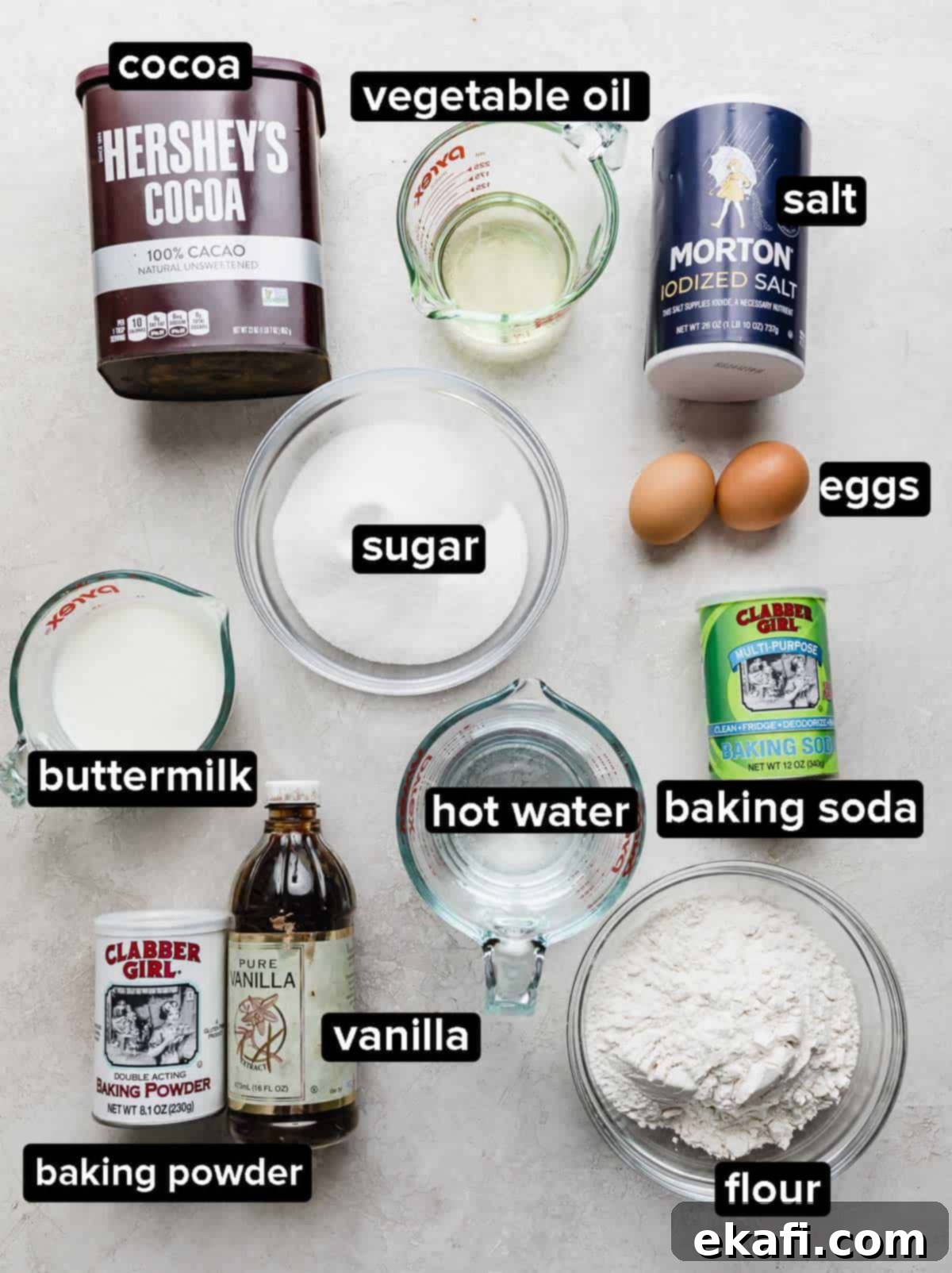 Chocolate Poke Cake 3 Various ingredients for chocolate poke cake, including cocoa powder, flour, sugar, buttermilk, and eggs, neatly arranged in glass bowls on a white background, highlighting fresh, quality components.