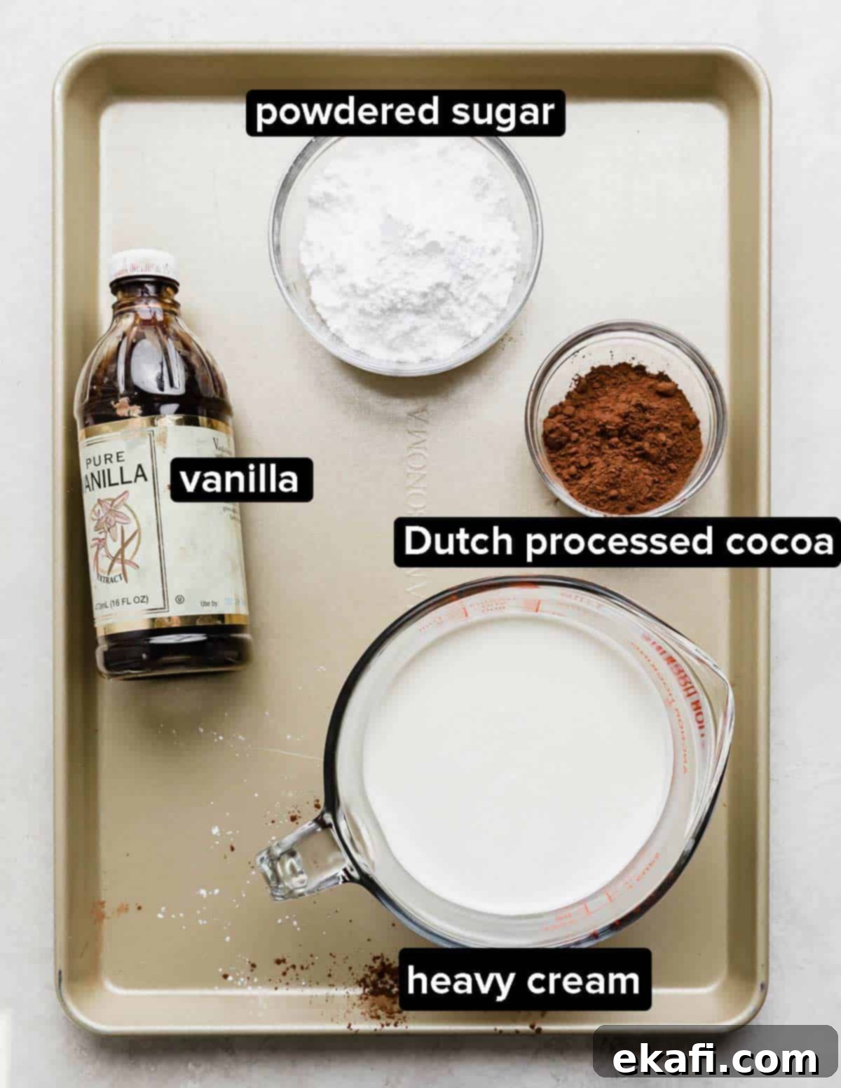 Chocolate Poke Cake 5 Key ingredients for luscious chocolate whipped cream: heavy cream, vanilla extract, Dutch-processed cocoa powder, and powdered sugar, arranged on a gold baking sheet, emphasizing freshness.