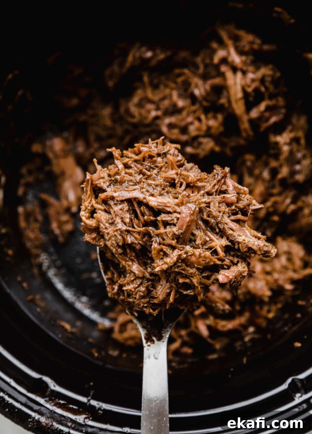 Fall-Apart Tender Slow Cooker Beef Tacos 5 Crock Pot Shredded Beef Taco meat balancing on a spoon over a black crock pot.
