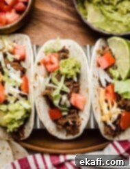 Fall-Apart Tender Slow Cooker Beef Tacos 7 Three flour tortillas filled with Crock Pot Shredded Beef Taco mix, shredded lettuce, guacamole, and tomatoes.