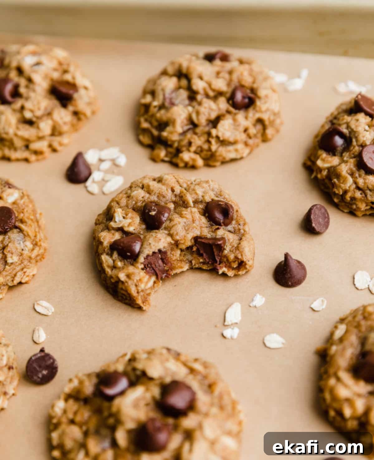 Cozy Pumpkin Chocolate Chip Oatmeal Delights 7 A delicious Chocolate Chip Oatmeal Pumpkin Cookie with a bite taken out of it, resting on a Kraft parchment-lined baking sheet.