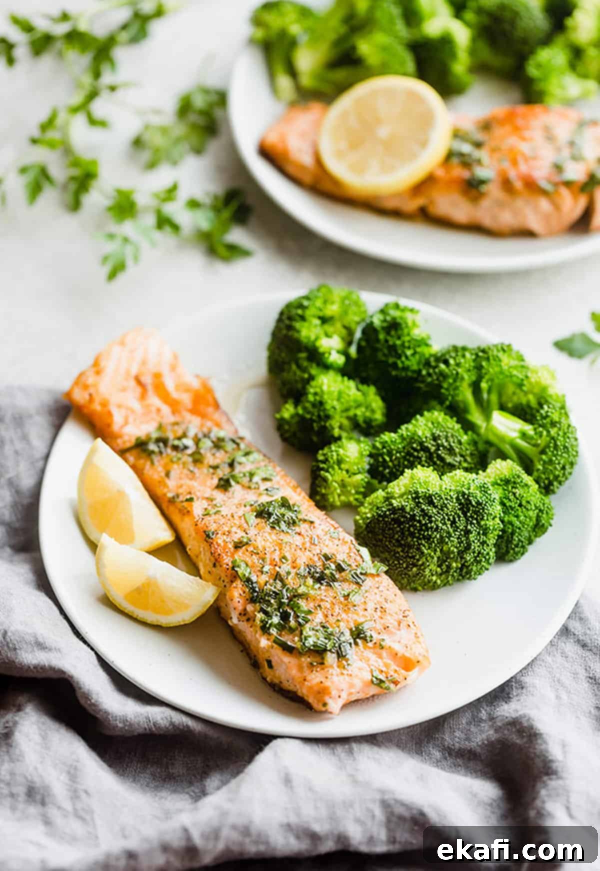 Delicious pan-seared Lemon Honey Glazed Salmon with fresh parsley, chives, and lemon. An easy and healthy dinner recipe for any night of the week. #saltandbaker #salmon #healthyrecipes A perfectly seared Lemon Honey Glazed Salmon fillet on a white plate, garnished with fresh herbs.