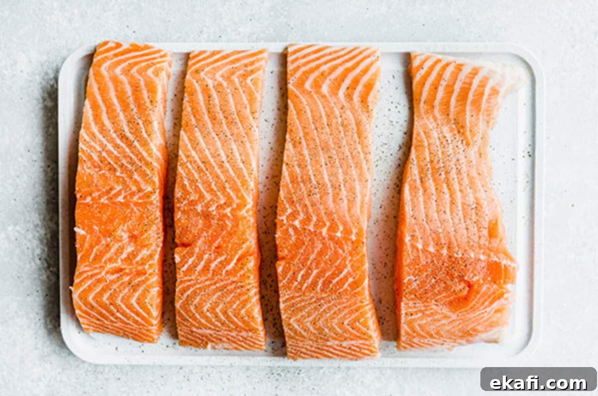 Raw salmon fillets seasoned and prepared for pan-searing, ensuring a perfect cook for Lemon Honey Glazed Salmon. #saltandbaker #salmonprep Four raw salmon fillets, seasoned with salt and pepper, on a white cutting board, ready for searing.
