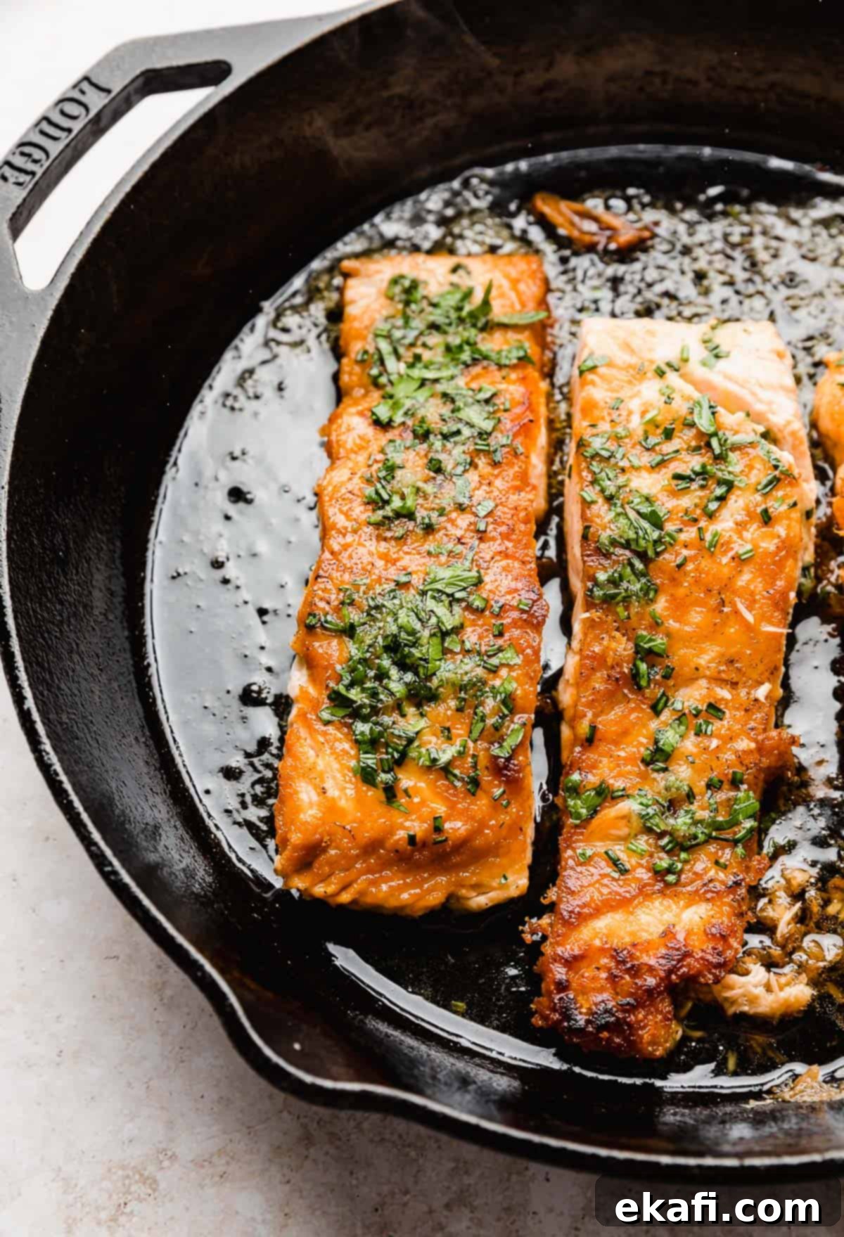 Sweet and Zesty Glazed Salmon 5 A close-up of seared Lemon Honey Glazed Salmon in a black skillet, drizzled with sauce and fresh herbs.