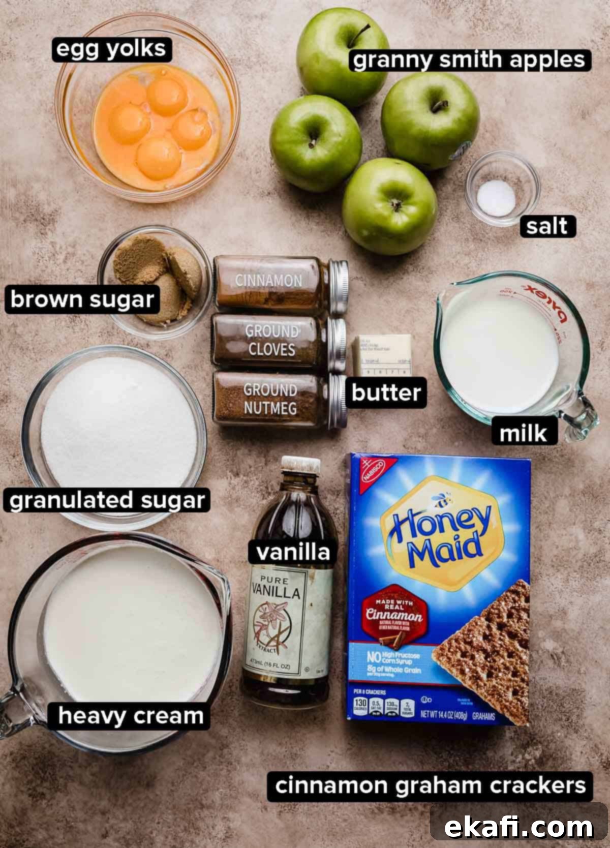 Παγωτό Μηλόπιτα 3 Συστατικά συνταγής Apple Pie Ice Cream σε μια ανοιχτόχρωμη καφέ ανάγλυφη επιφάνεια: Μήλα Granny Smith, κανέλα, κρέμα γάλακτος, κρόκοι αυγών, ζάχαρη, μπαχαρικά και κράκερς κανέλας γκράχαμ.