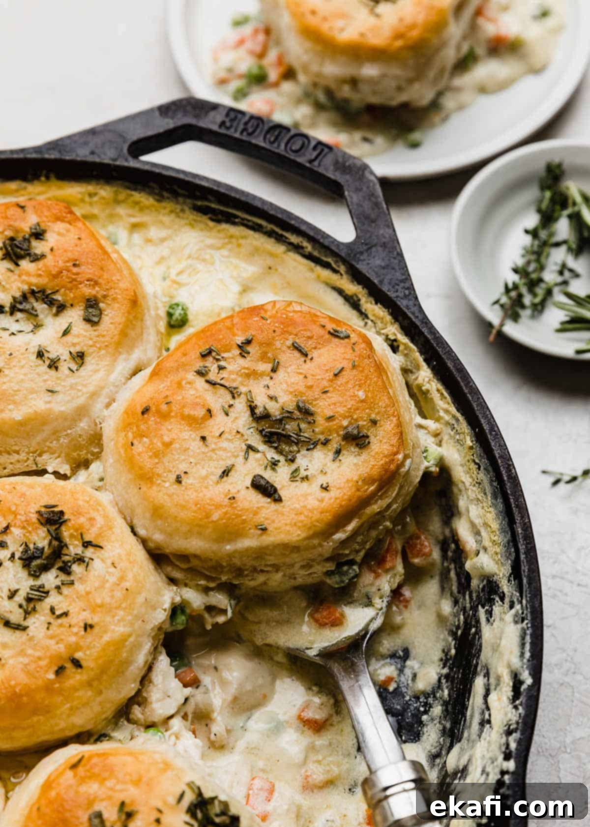 Cast Iron Chicken Pot Pie 2 Flaky biscuits atop a chicken pot pie filling in a cast iron skillet on a light gray background.