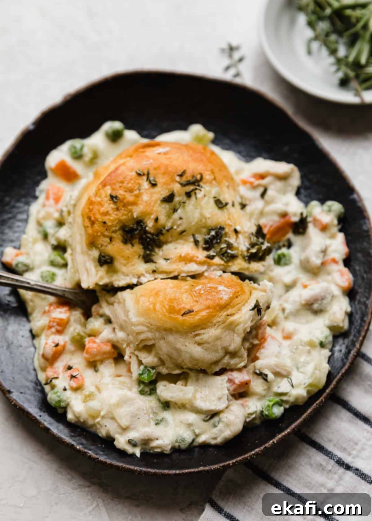 Cast Iron Chicken Pot Pie 8 A biscuit and chicken pot pie mixture on a black plate with a fork cutting into the biscuit.