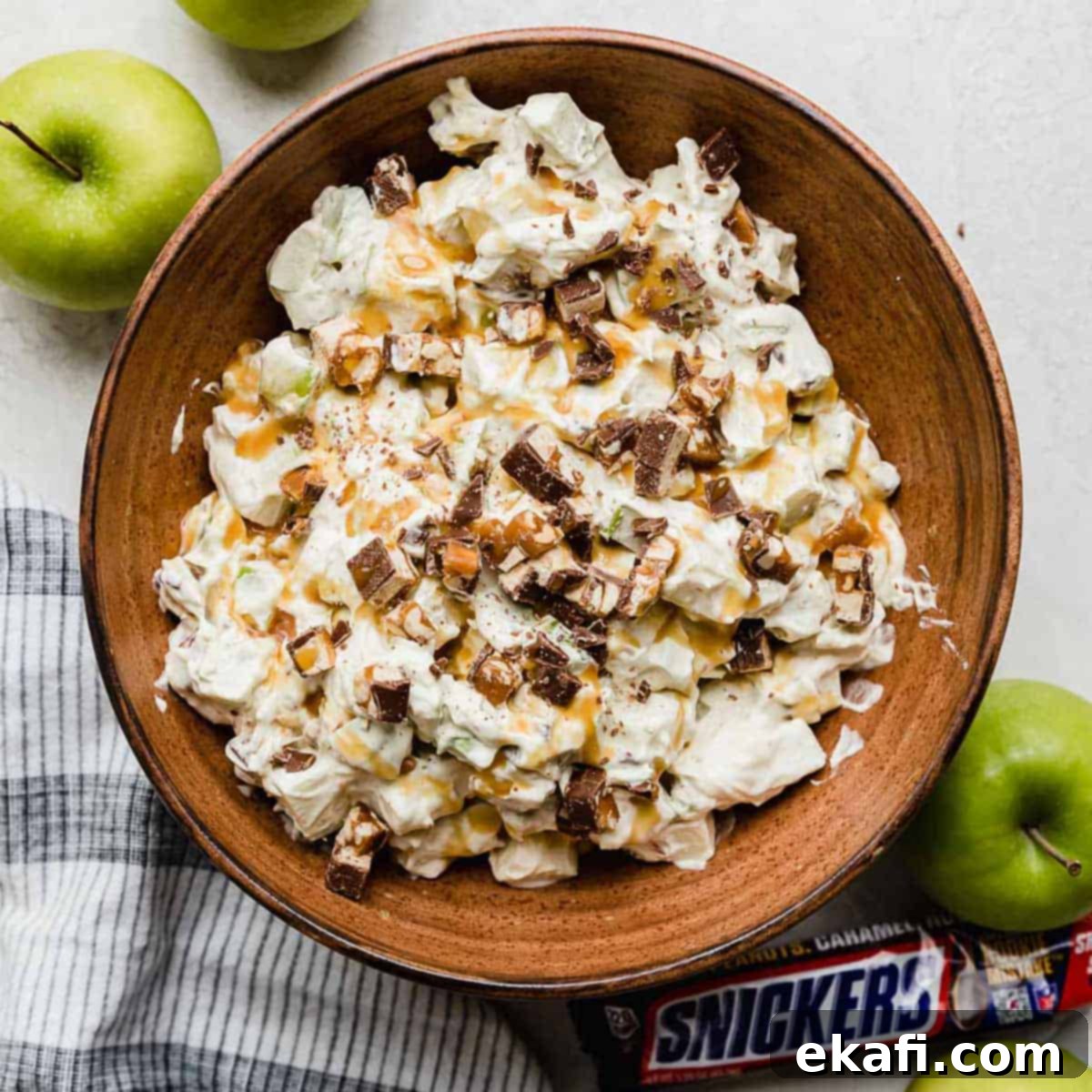 Creamy Snickers Apple Delight 7 Overhead photo of a salad with snickers and apples in a brown bowl topped with caramel to make the best Apple Snickers Salad recipe.