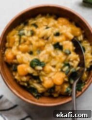 Creamy Butternut Squash Orzo 9 Brown bowl filled with Butternut Squash Orzo pasta with kale and sage brown butter sauce, on a light gray surface.