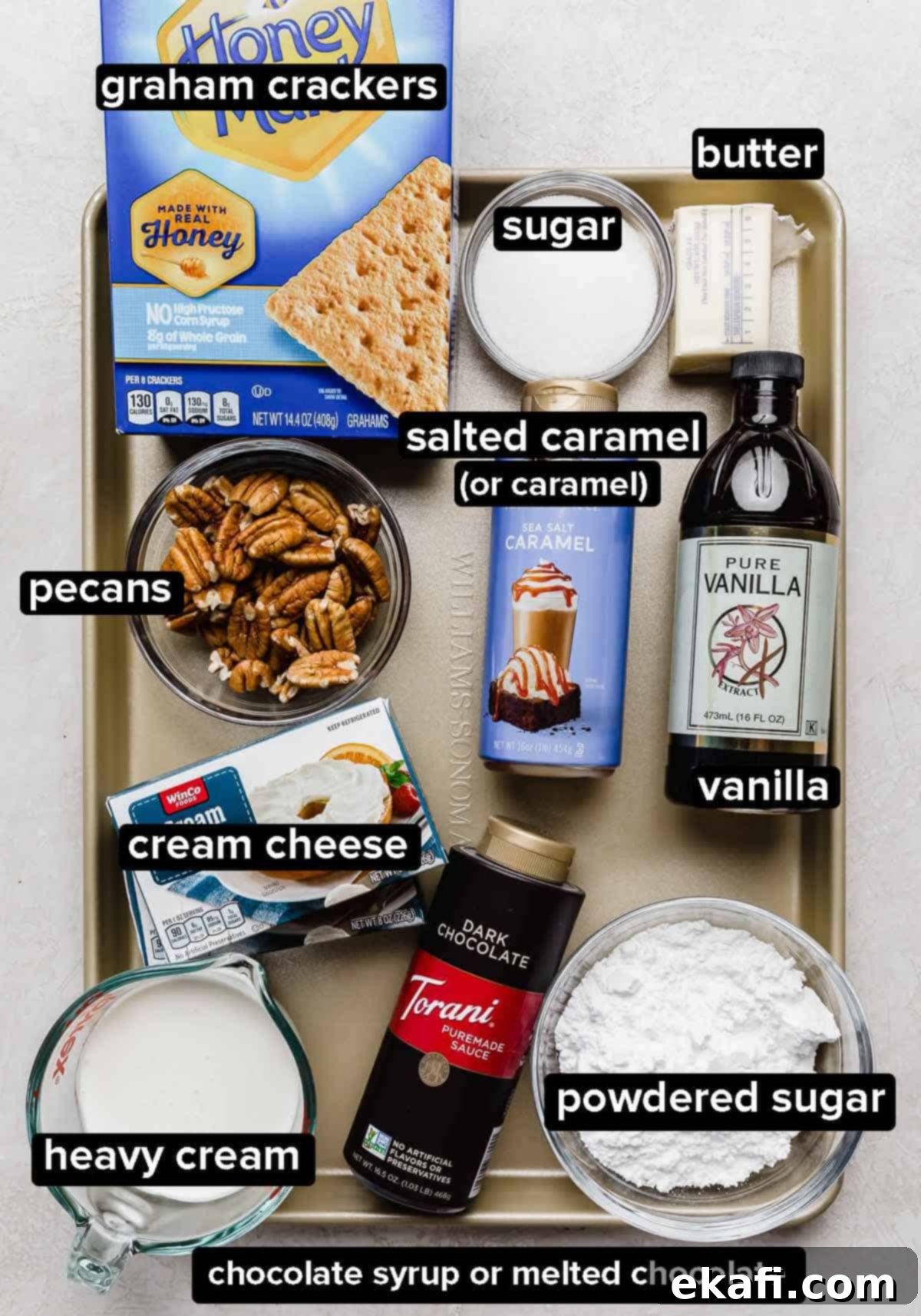 Caramel Pecan Utopia 3 The best Turtle Pie recipe ingredients on a gold baking sheet: salted caramel, pecans, sugar, graham crackers, cream cheese, heavy cream, vanilla and butter.