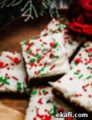 Soft & Chewy Gingerbread Bars 9 Gingerbread Cookie Bars topped with cream cheese frosting and red and green sprinkles, on a brown plate.