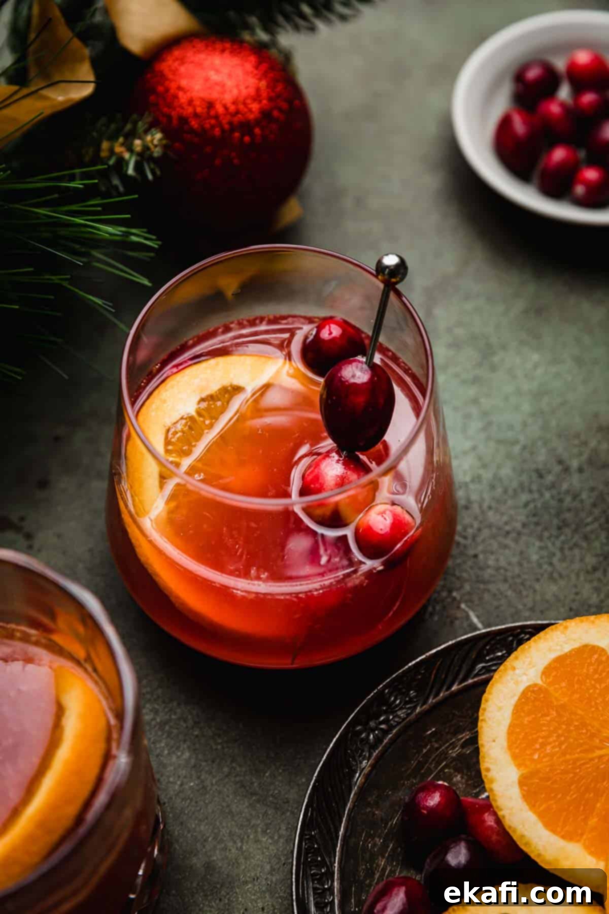Παρθένο Κράνμπερι Κοκτέιλ 5 Ένα cranberry πορτοκαλί mocktail σε ένα γυάλινο ποτήρι σε πράσινη επιφάνεια με μια φέτα πορτοκαλιού και φρέσκα κράνμπερι να γαρνίρουν το ποτό.