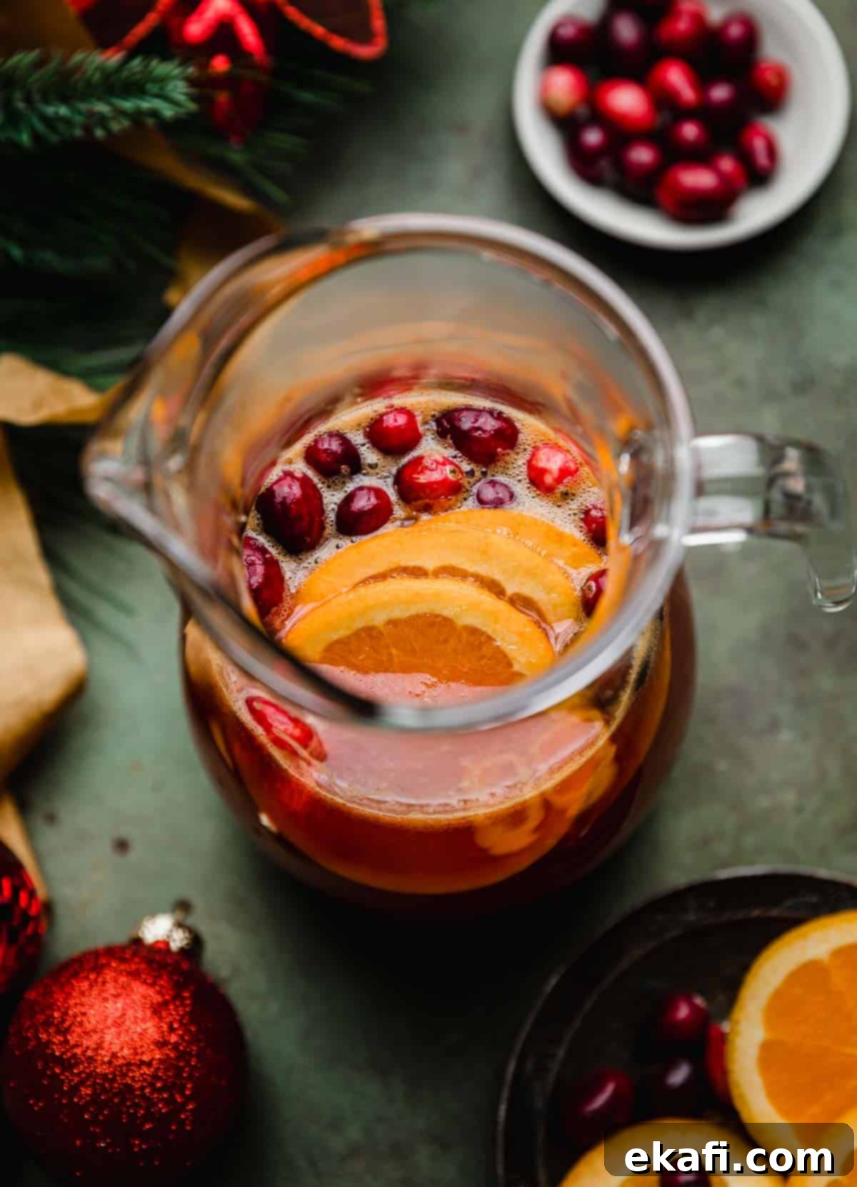 Παρθένο Κράνμπερι Κοκτέιλ 6 Μια συνταγή για cranberry πορτοκαλί mocktail σε γυάλινη κανάτα σε φόντο πράσινο του δάσους.
