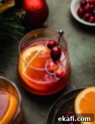 Παρθένο Κράνμπερι Κοκτέιλ 7 Ένα cranberry πορτοκαλί mocktail σε ένα γυάλινο ποτήρι σε πράσινη επιφάνεια με μια φέτα πορτοκαλιού και φρέσκα κράνμπερι να γαρνίρουν το ποτό.