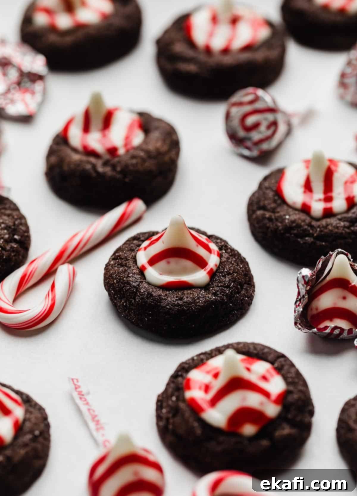 Peppermint Kissed Chocolate Gems 2 Chocolate Peppermint Blossoms cookies topped with a candy cane kiss on a white background.