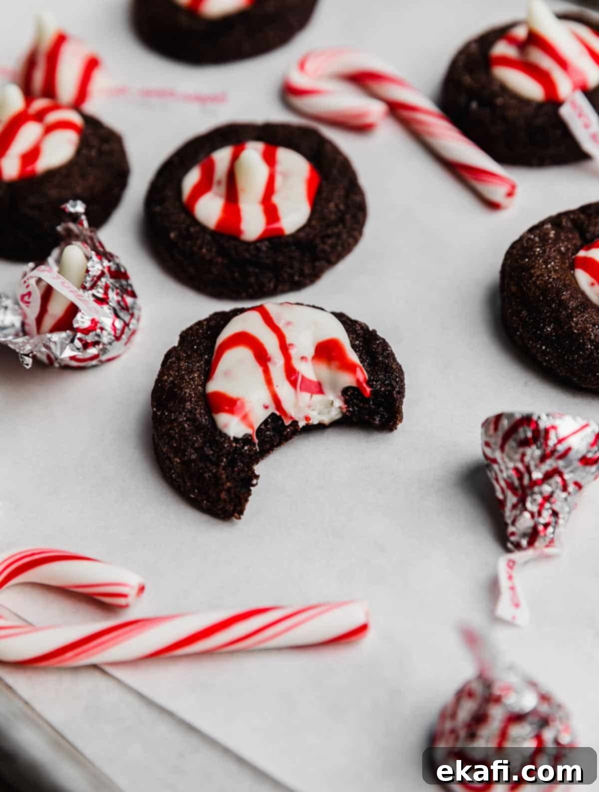 Peppermint Kissed Chocolate Gems 6 A chocolate peppermint blossom cookie on a white parchment paper with a bite taken out of the cookie.
