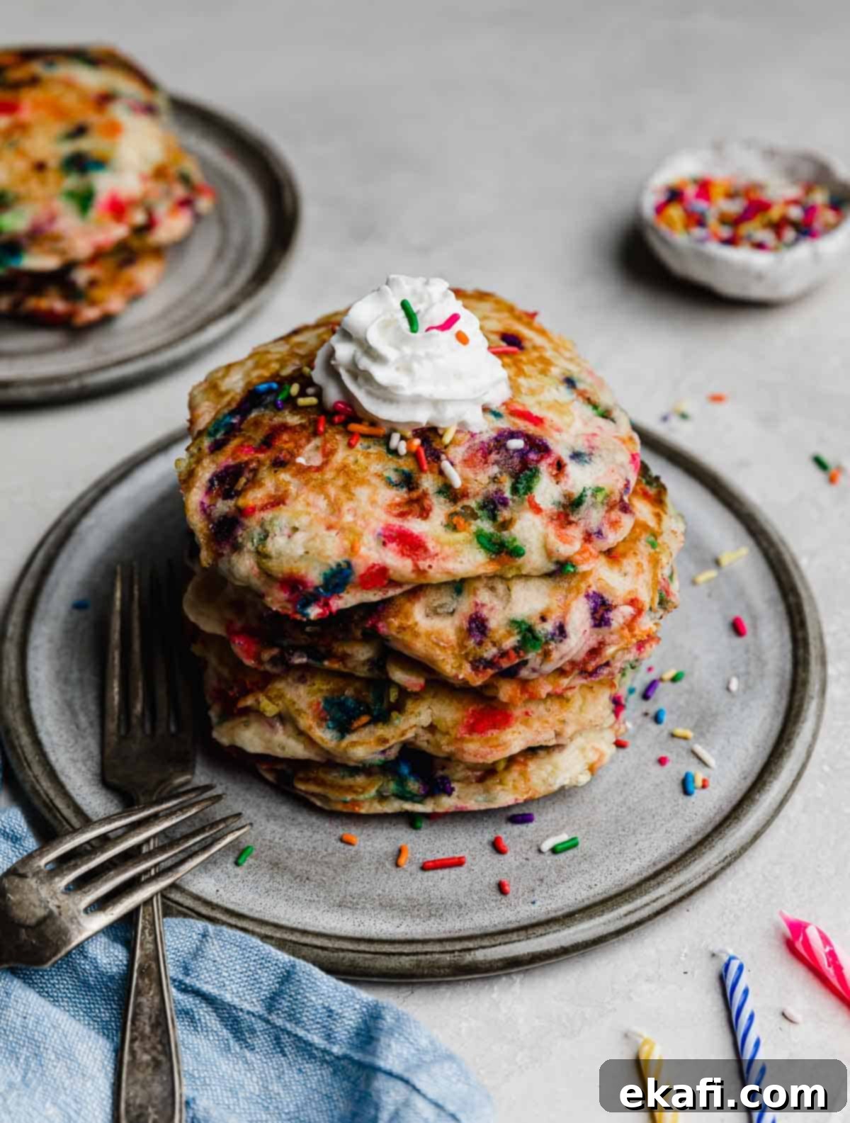 Confetti Morning Cakes 7 Birthday Cake Pancakes on a gray plate on a light gray background with birthday candles next to the plate.