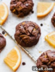 Irresistible Chocolate Orange Cookies 9 Chocolate Orange Cookies on a wire rack surrounded by fresh orange slices.