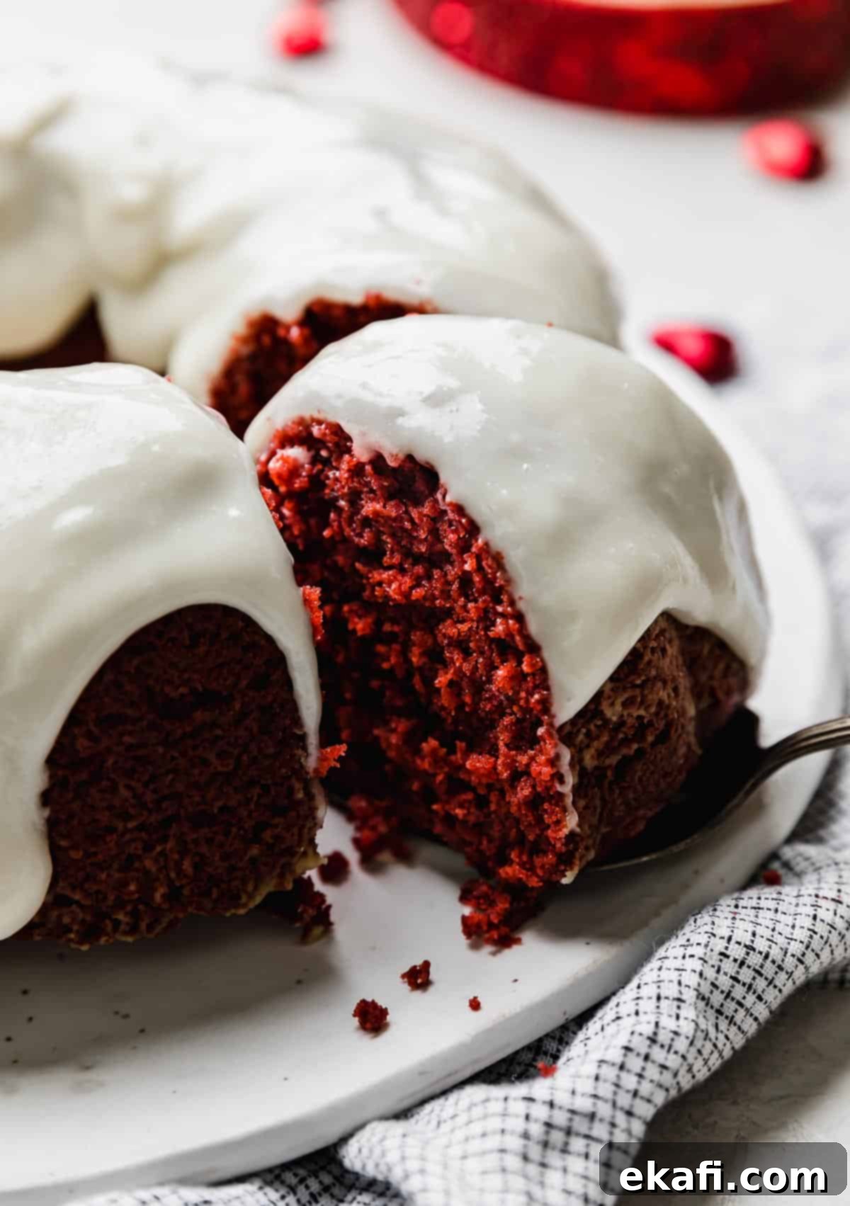Velvety Crimson Crown 2 A moist Red Velvet Bundt Cake topped with cream cheese glaze and a slice of cake partially removed from the red bundt cake, highlighting its rich color and tender texture.