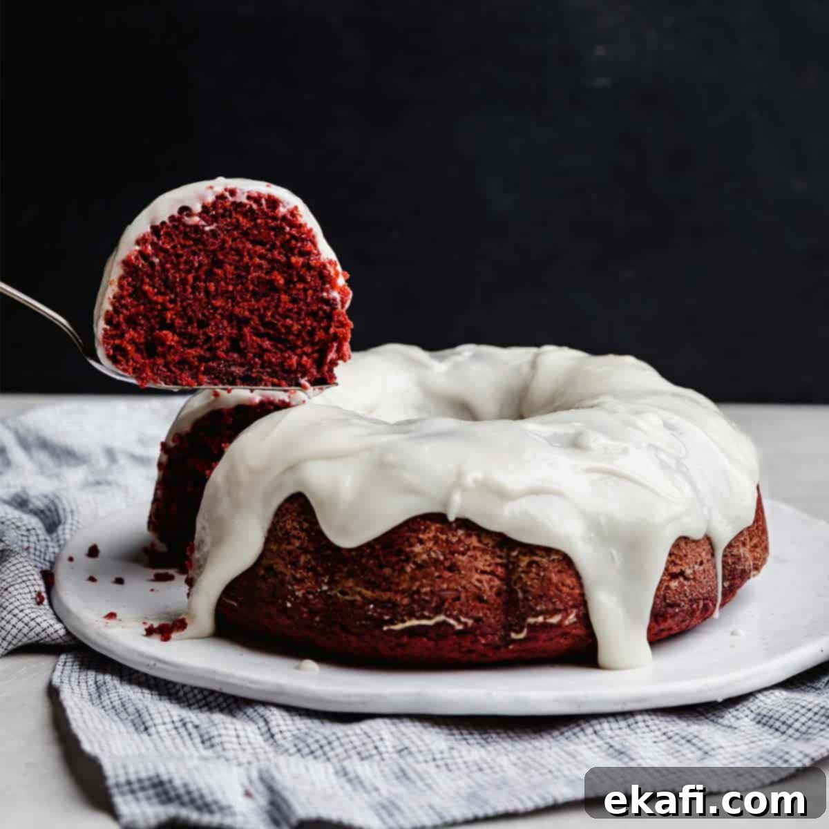 Velvety Crimson Crown 7 A vibrant slice of red velvet bundt cake with glaze, artfully hovering above the complete cream cheese glaze topped Red Velvet Bundt Cake, set against a dramatic black background, perfect for a Valentine's Day dessert.