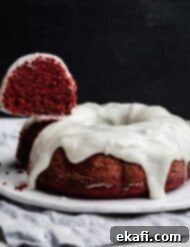 Velvety Crimson Crown 10 A slice of red valentines day bundt cake hovering over a cream cheese glaze topped Red Velvet Bundt Cake against a black background, representing the final delicious product.