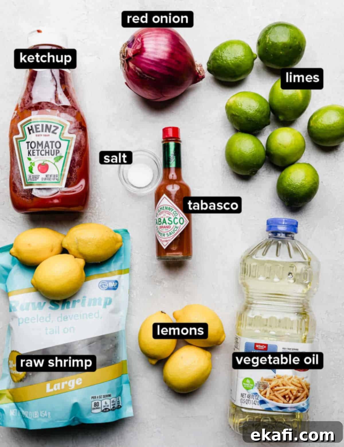 Refreshing Cooked Shrimp Ceviche 3 Shrimp Ceviche recipe ingredients on a white surface: ketchup, oil, fresh lemons and limes, tabasco, raw shrimp, and salt.