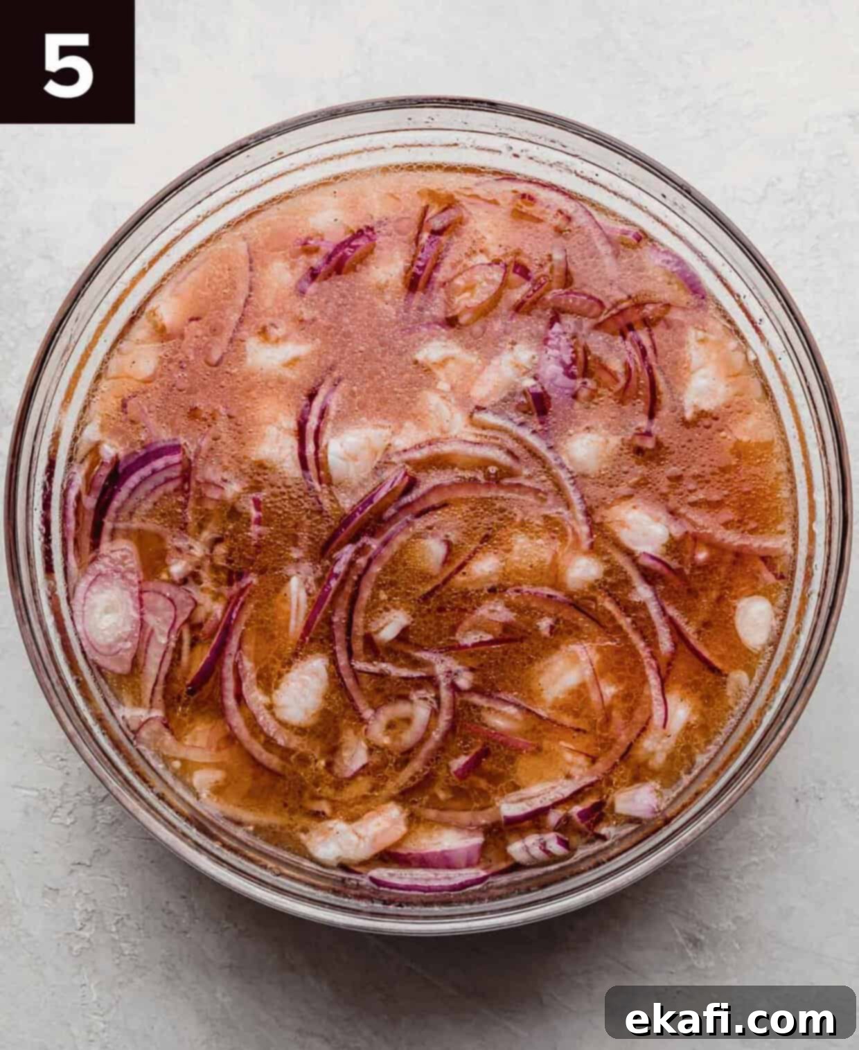 Refreshing Cooked Shrimp Ceviche 5 Cooked shrimp, purple onion, and acidic mixture in a glass bowl.