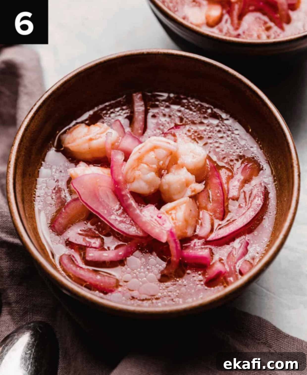 Refreshing Cooked Shrimp Ceviche 6 A Shrimp Ceviche soup with purple onions in a brown bowl on a light gray surface.