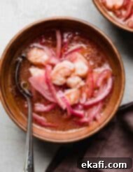 Refreshing Cooked Shrimp Ceviche 8 Shrimp Ceviche with sliced purple onions in a ketchup and tabasco based lemon lime sauce, in a bowl on a light gray surface.