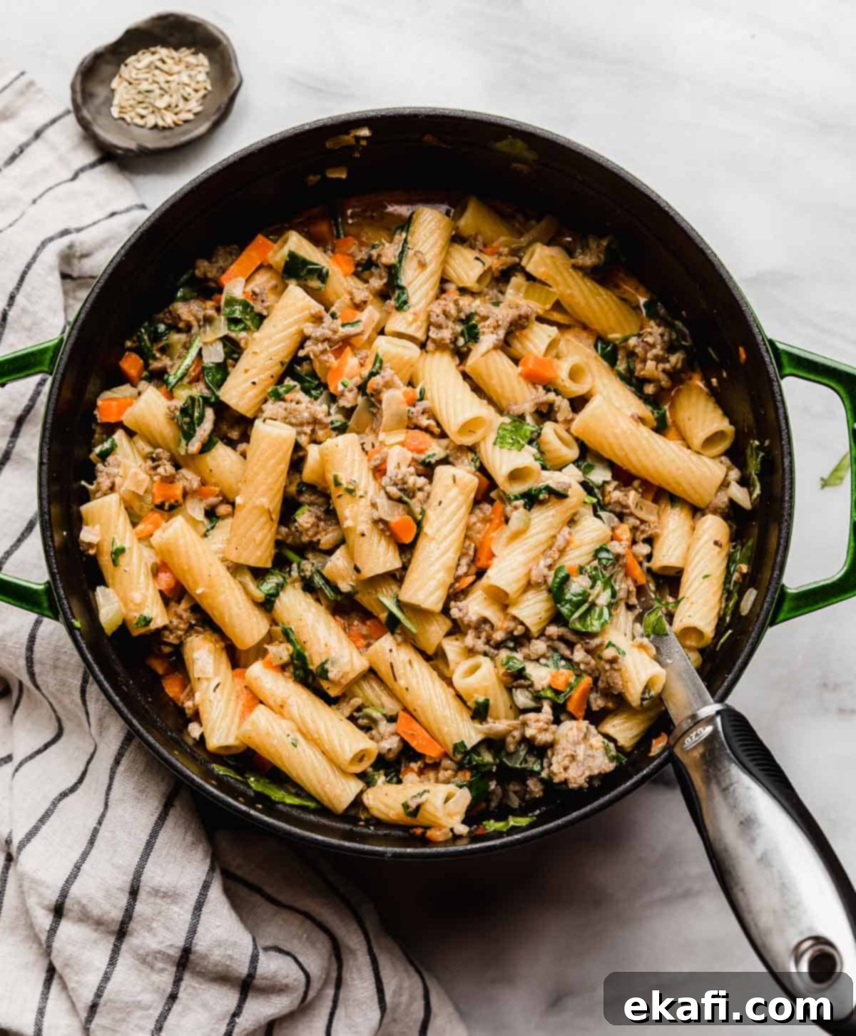 Italian Sausage Rigatoni 2 A green dutch oven filled with Italian Sausage Rigatoni with spinach on a white marble surface.