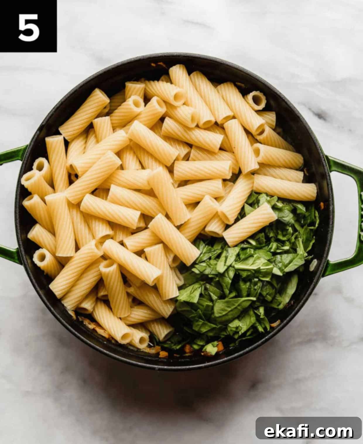 Italian Sausage Rigatoni 5 Cooked rigatoni noodles and chopped spinach in a large dutch oven on a white surface.