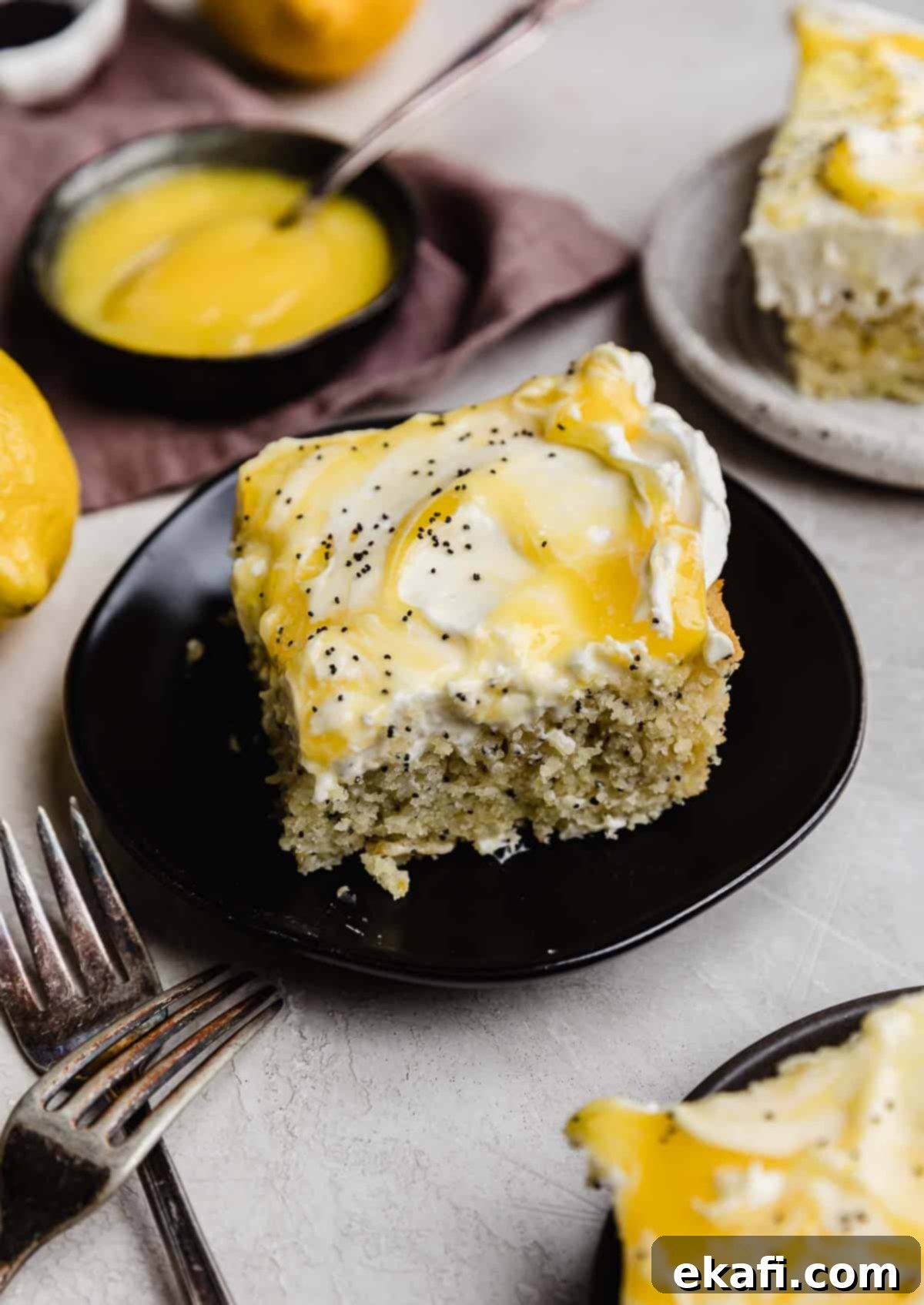 Sunshine Lemon Poppy Seed Cloud Cake 8 A lemon poppy seed sheet cake cut into a square on a black plate.