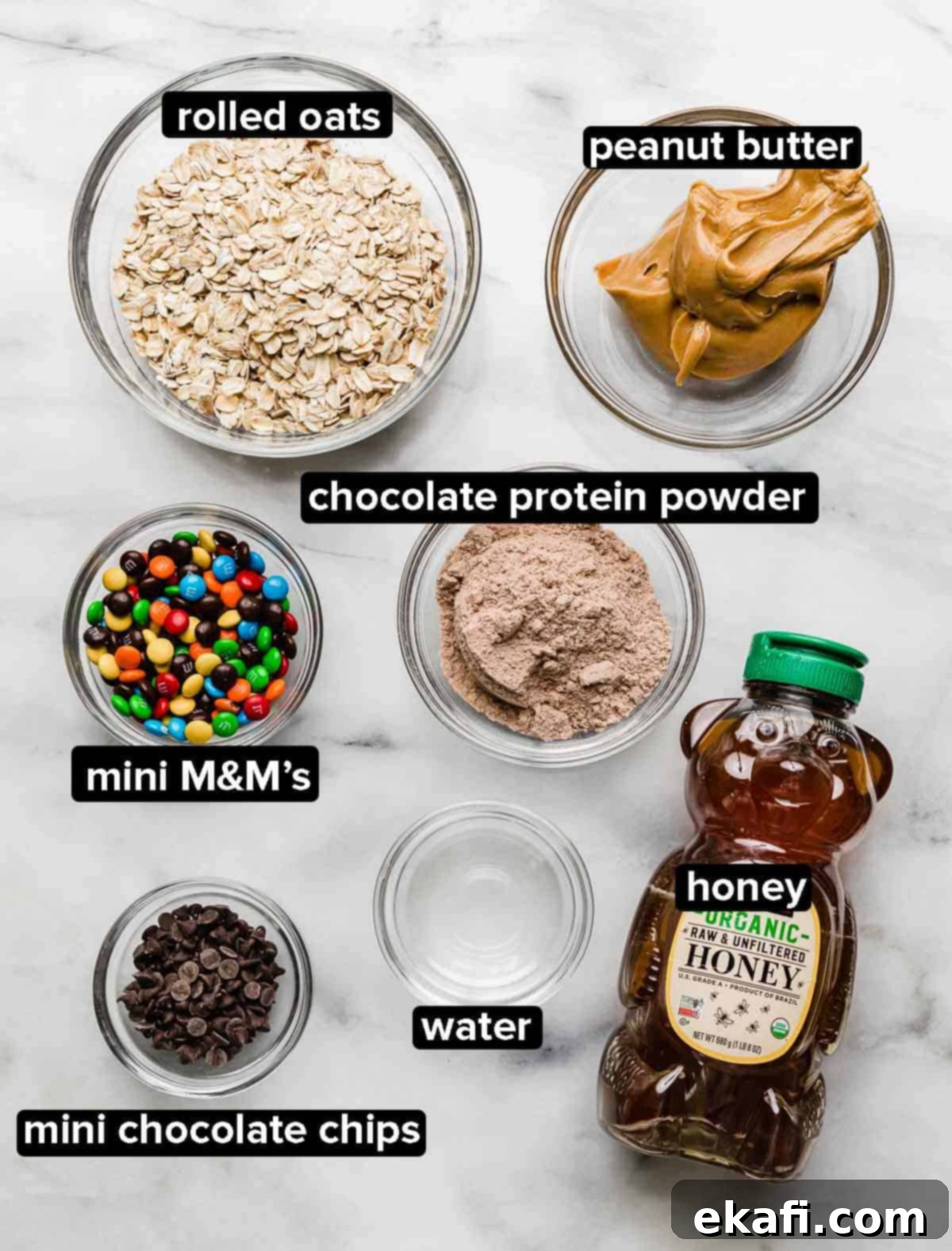 Monster Cookie Protein Bites 3 Monster Cookie Protein Balls recipe ingredients on a white background: oats, peanut butter, honey, chocolate protein powder, mini M&M's, water, and mini chocolate chips.