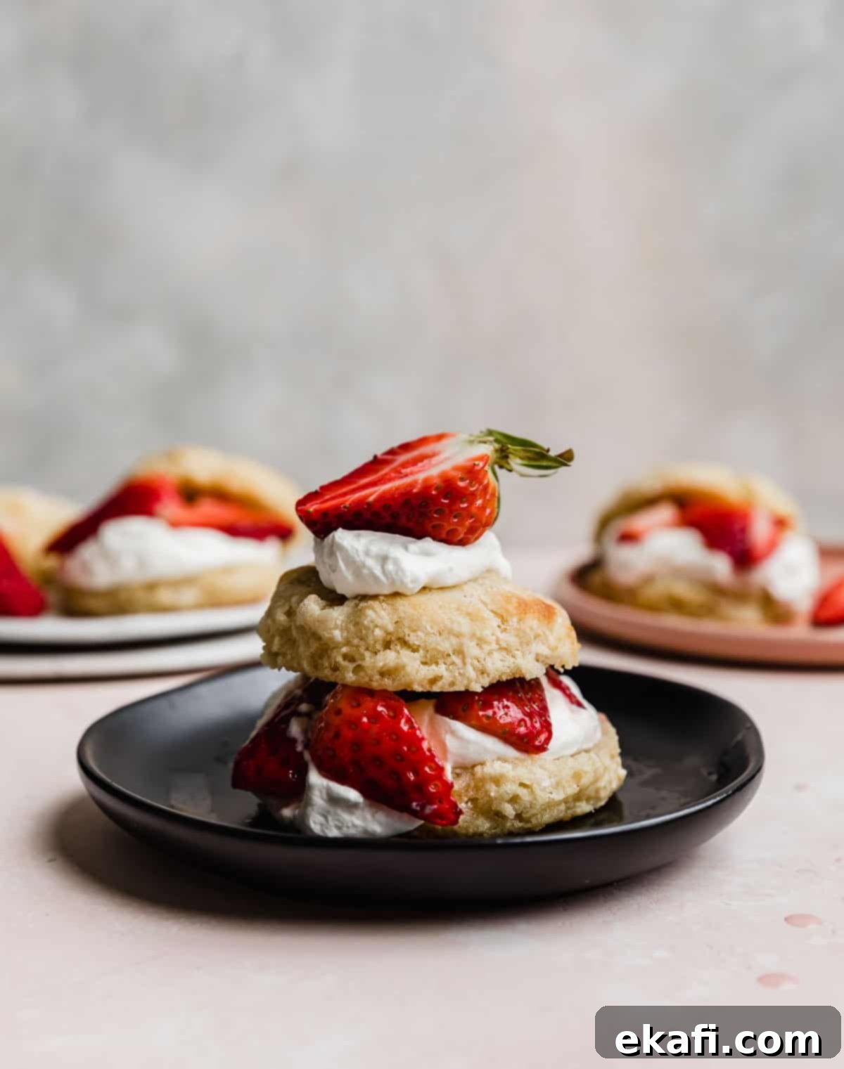 Grandma's Strawberry Shortcake 2 A Classic Strawberry Shortcake biscuit cut in half, topped with freshly whipped cream, sugared strawberries, on a black plate.