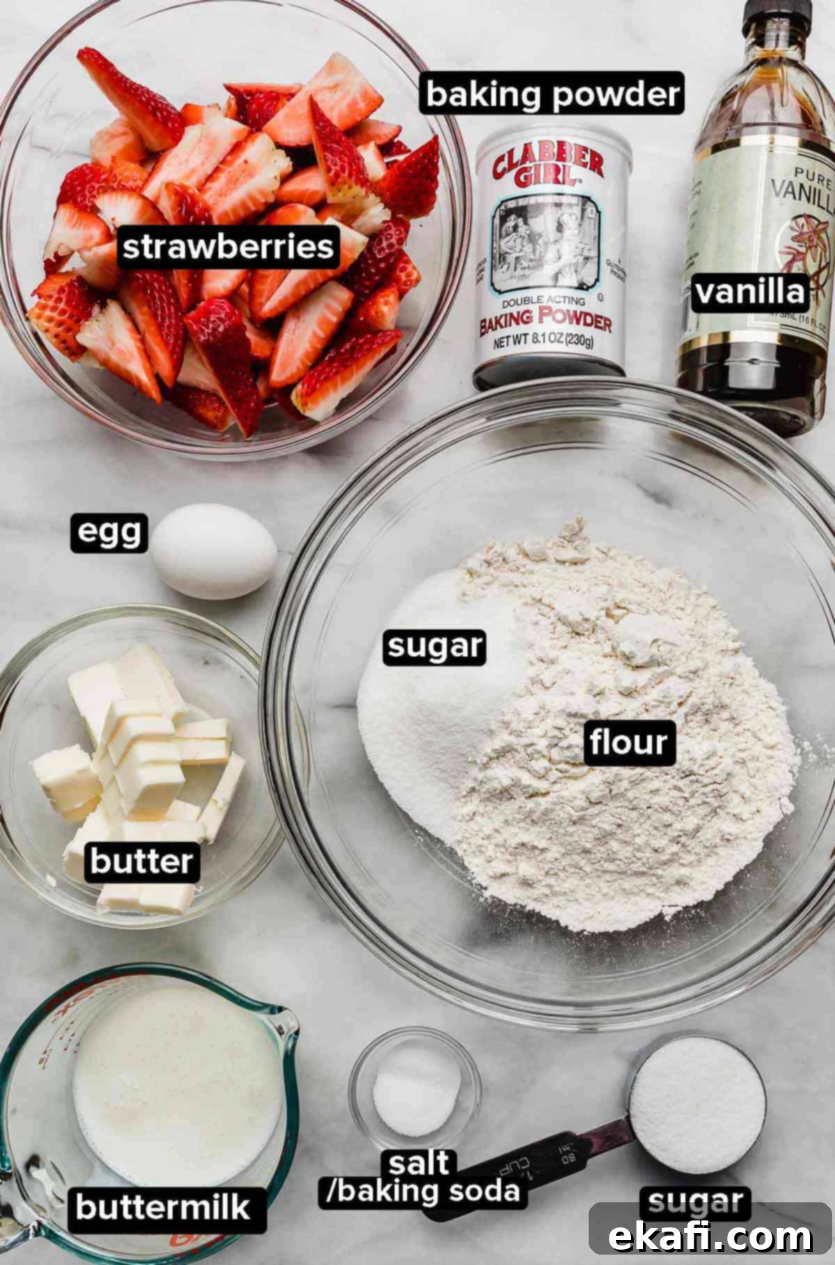 Grandma's Strawberry Shortcake 3 Classic Strawberry Shortcake recipe ingredients portioned into glass bowls on a white marble surface: strawberries, flour, sugar, buttermilk, butter, egg, salt, baking powder, baking soda, and vanilla.