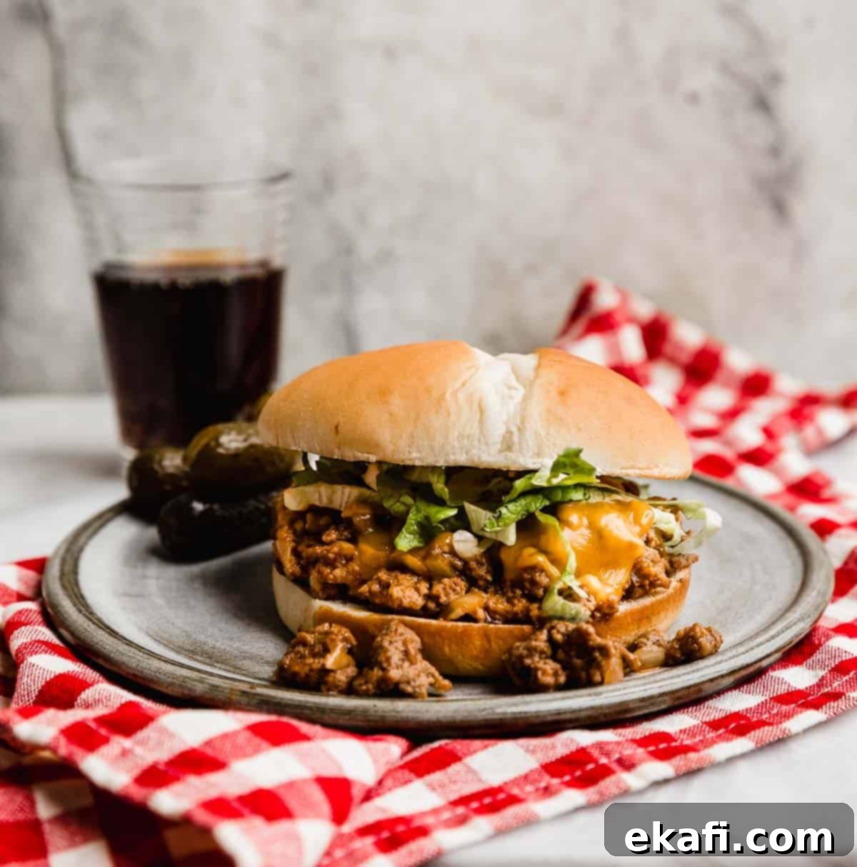 Χαμός Τυρο-Μπέργκερ 2 Ένα Cheeseburger Sloppy Joe σε ένα γκρι πιάτο με λιωμένο τυρί και τριμμένο μαρούλι πάνω από το μείγμα sloppy Joe.