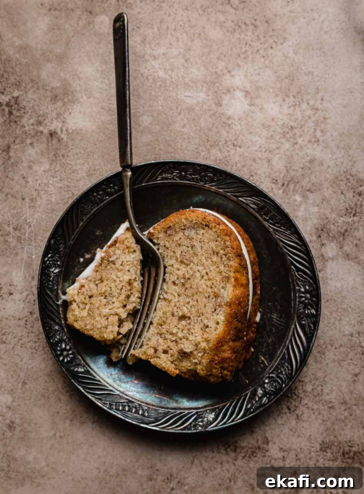 Classic Banana Bread Bundt Cake 6 A slice of Banana Bread Bundt Cake on a black antique plate with a fork cutting into the bundt cake.