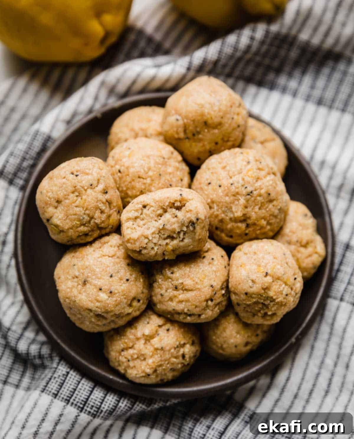 Zesty Lemon Protein Bites 2 A black plate piled with Lemon Protein Balls on it, garnished with fresh lemon zest and poppy seeds.