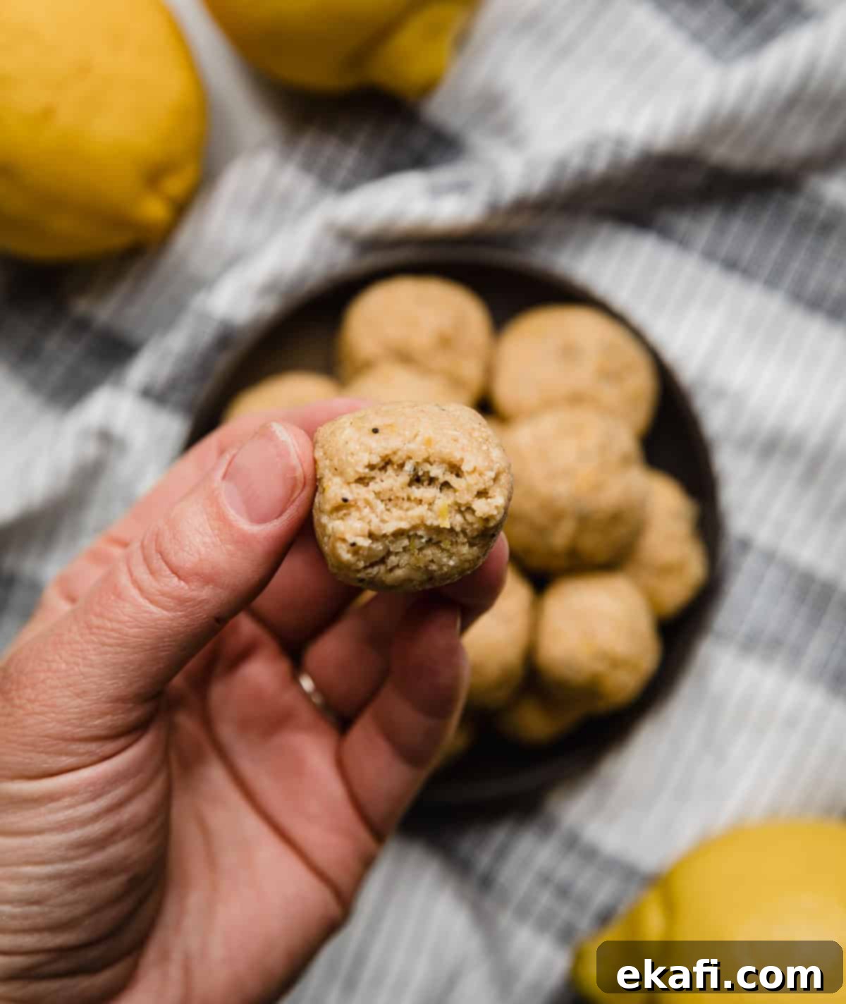 Zesty Lemon Protein Bites 5 A hand holding a Lemon Protein Bite with a bite taken out of the protein ball, showing the soft interior and poppy seeds.