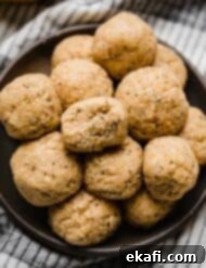 Zesty Lemon Protein Bites 6 A bite taken out of a Lemon Protein Ball that's stacked on a black plate with other lemon poppy seed protein balls.