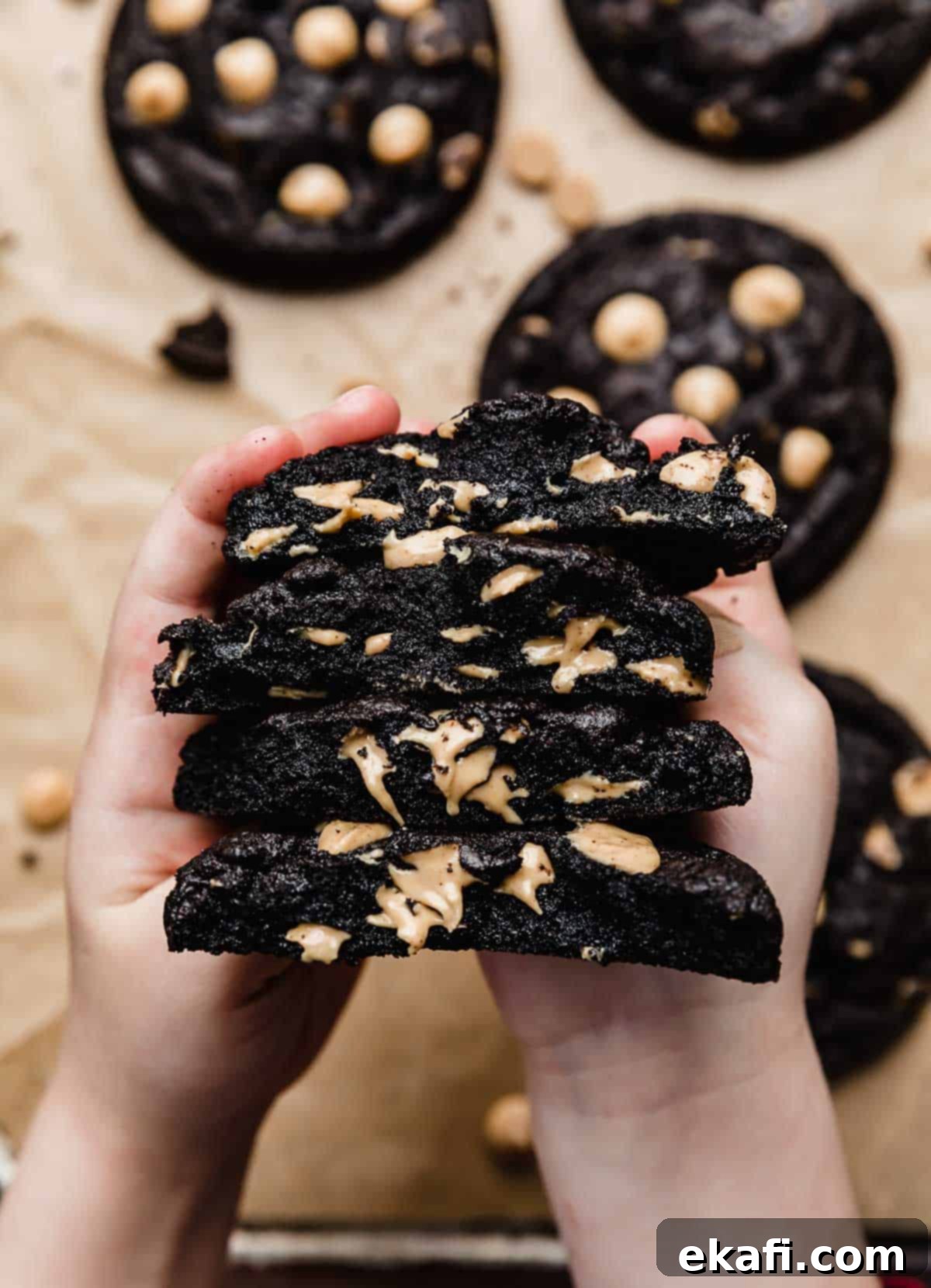 Ultimate Oreo Peanut Butter Cookies 2 Two small hands holding a stack of freshly baked Peanut Butter Oreo Cookies that have been cut in half, revealing the soft, chewy interior and peanut butter chips.