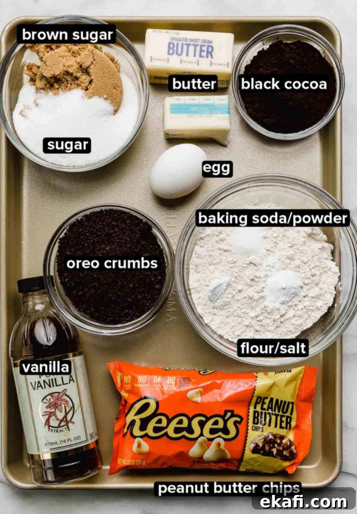 Ultimate Oreo Peanut Butter Cookies 3 A golden baking sheet filled with various ingredients for Peanut Butter Oreo Cookies, including peanut butter chips, flour, salt, baking powder and soda, vanilla extract, butter, eggs, and sugars, all neatly arranged.